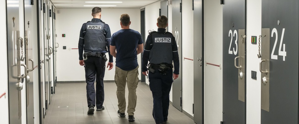Zwei Beamte begleiten einen Inhaftierten zum Haftraum